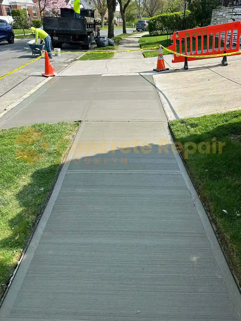 A dry concrete sidewalk section bordered by a green chain-link fence.